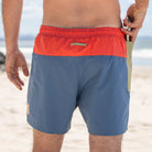 Back view of man wearing swim shorts putting phone into side pocket