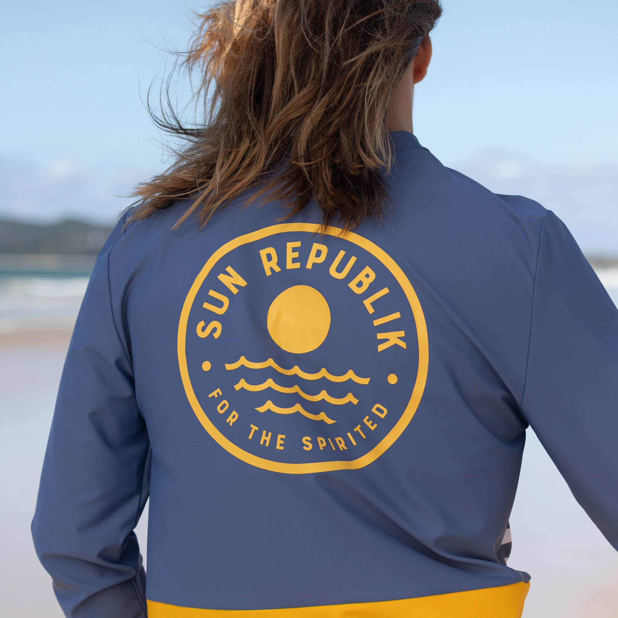 Man wearing mens beach wear swim top, long sleeve and large logo on back.