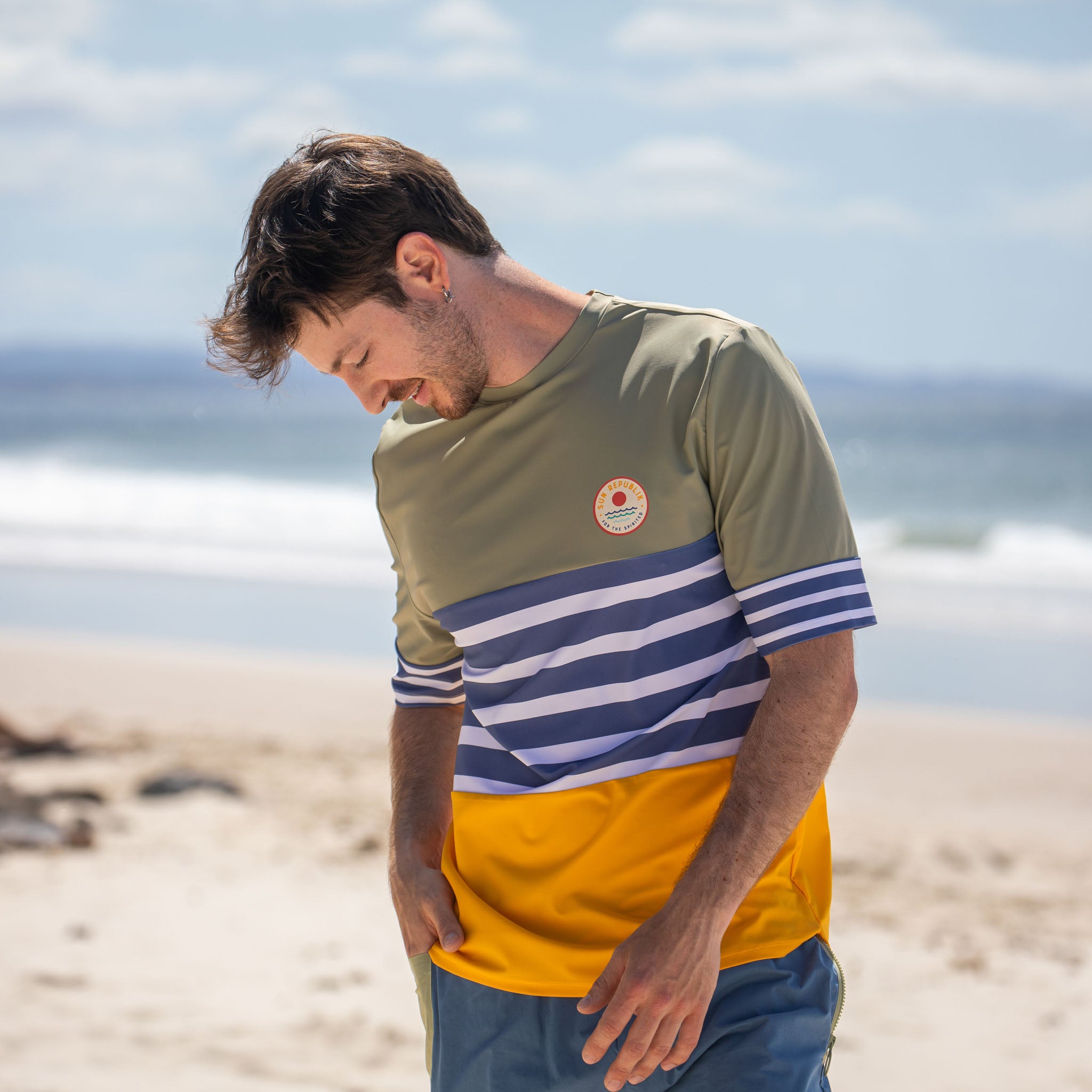 Man smiling on beach wearing men swimwear swim shirt, short sleeve and blue stripe.