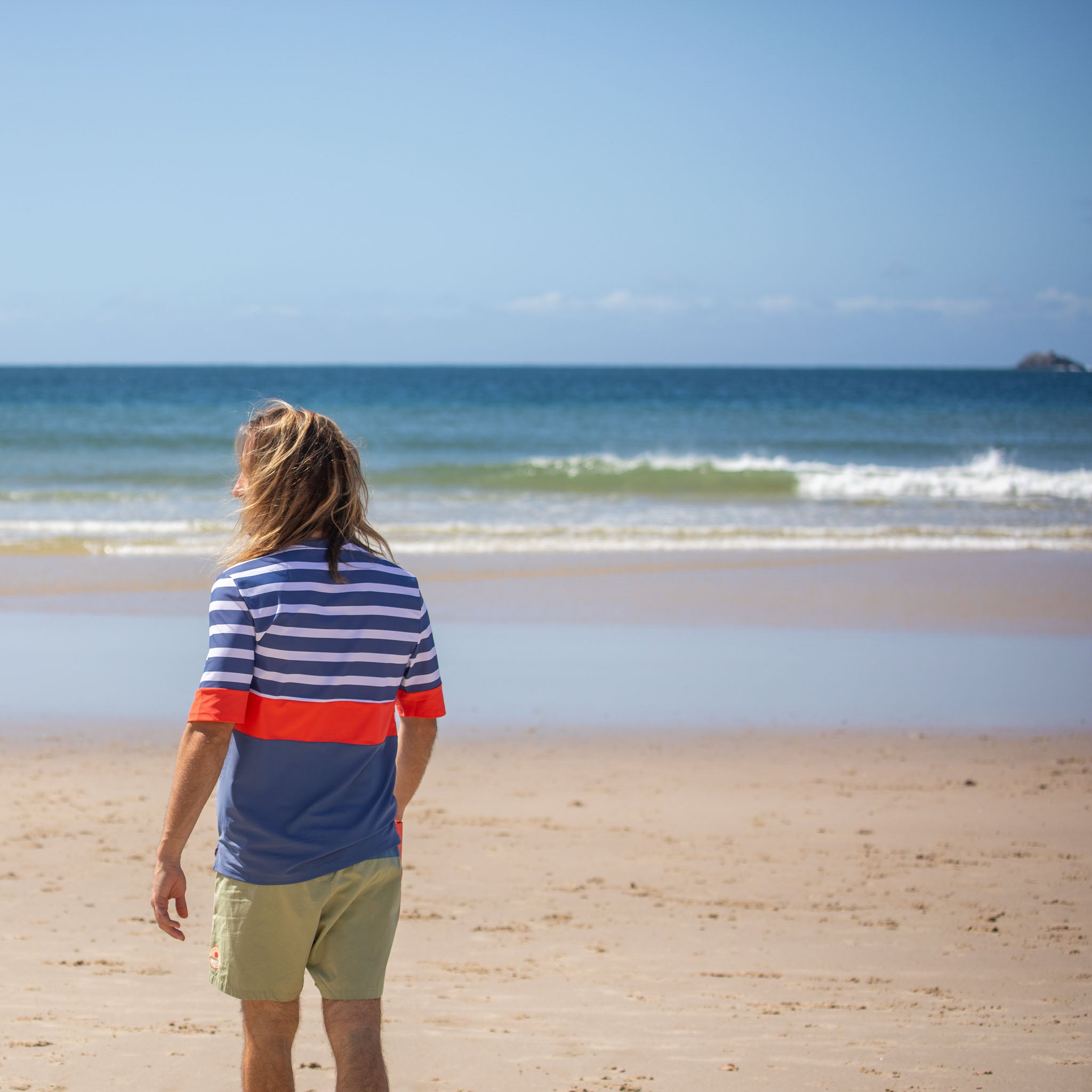 Back view of man standing on sand wearing mens beach wear swim top.