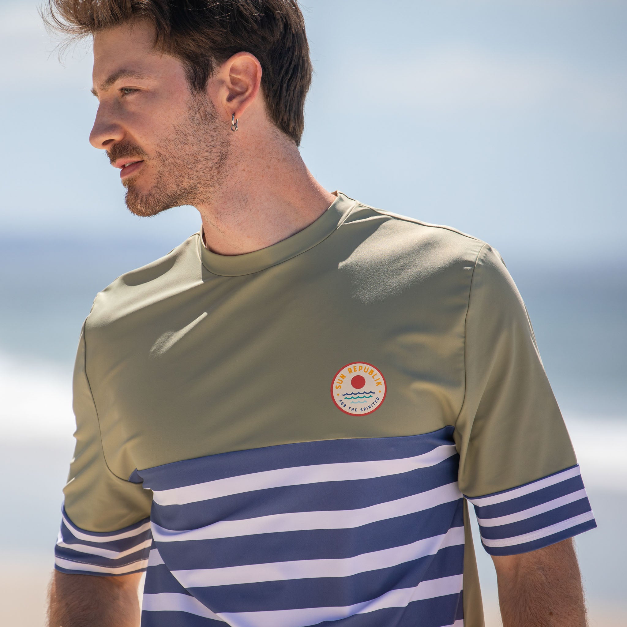 Man wearing mens beach wear short sleeve rash guard. Blue stripe and logo.