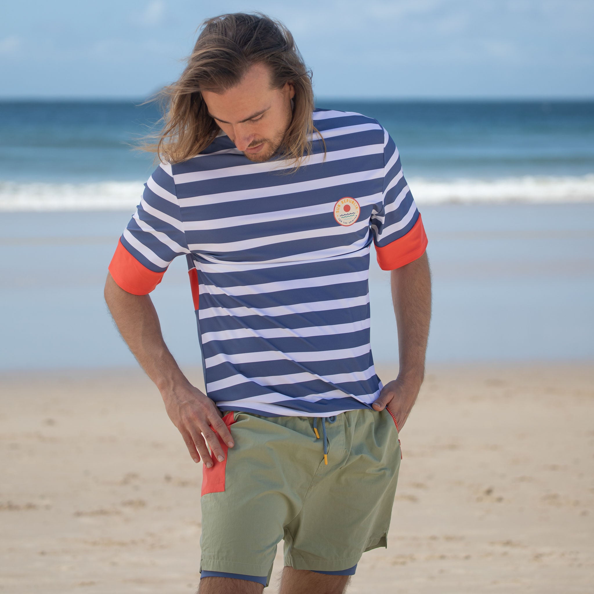 Man standing on beach wearing men swimwear rash guard and shorts.