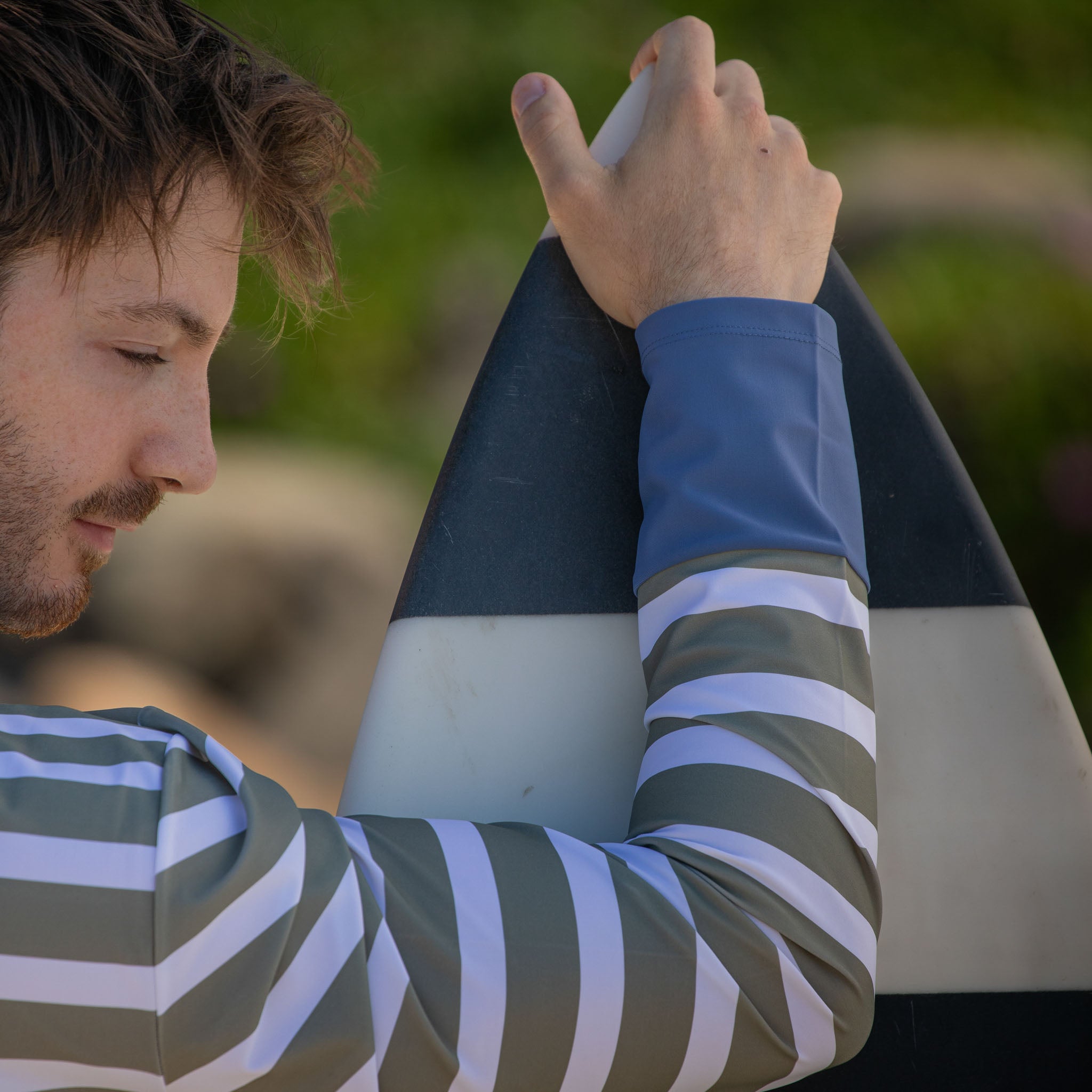 Man holding surf board showing cuff of beach wear swim shirts, long sleeve.