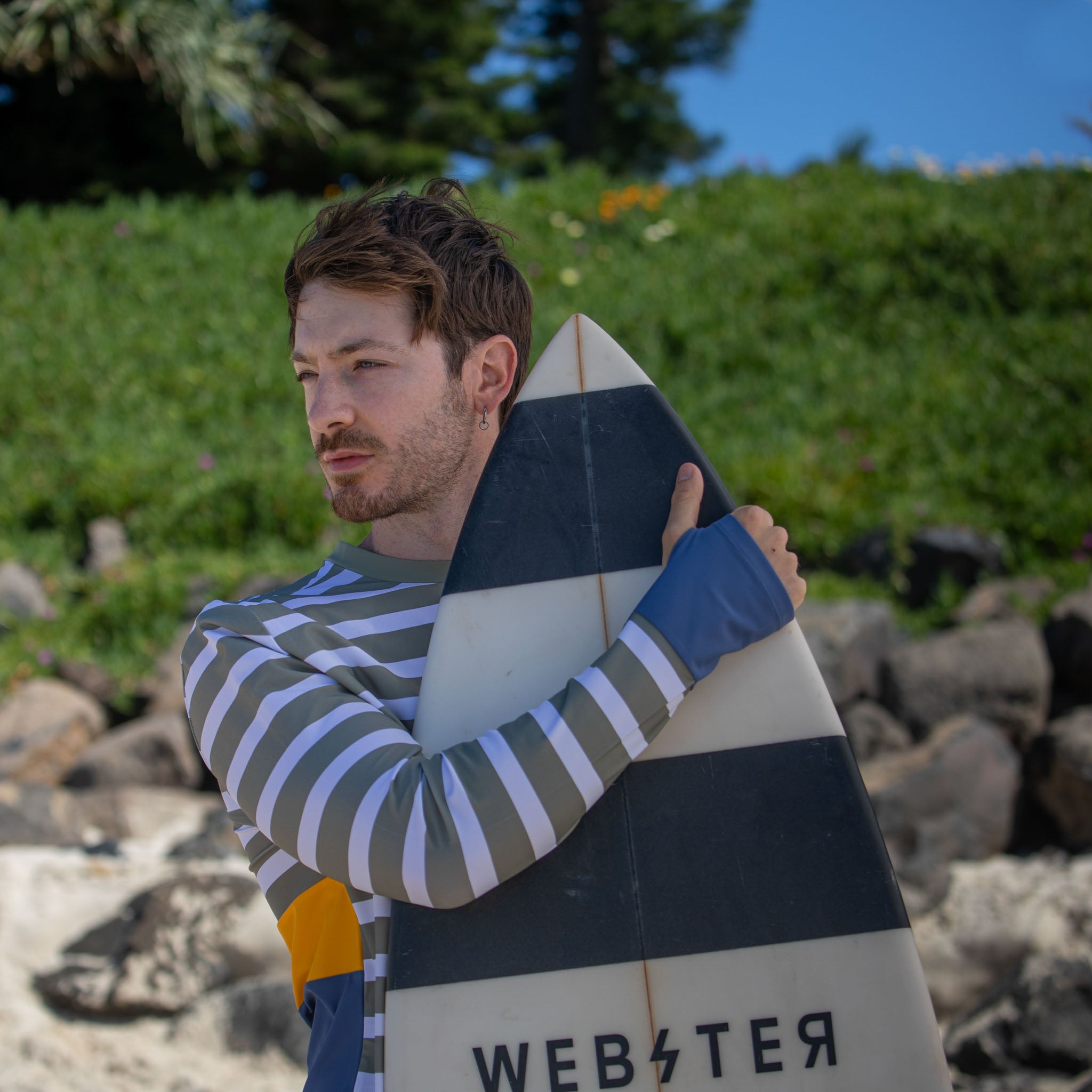 all-products Man holding surfboard wearing men swimwear rashie, long sleeve with cuff on hand.