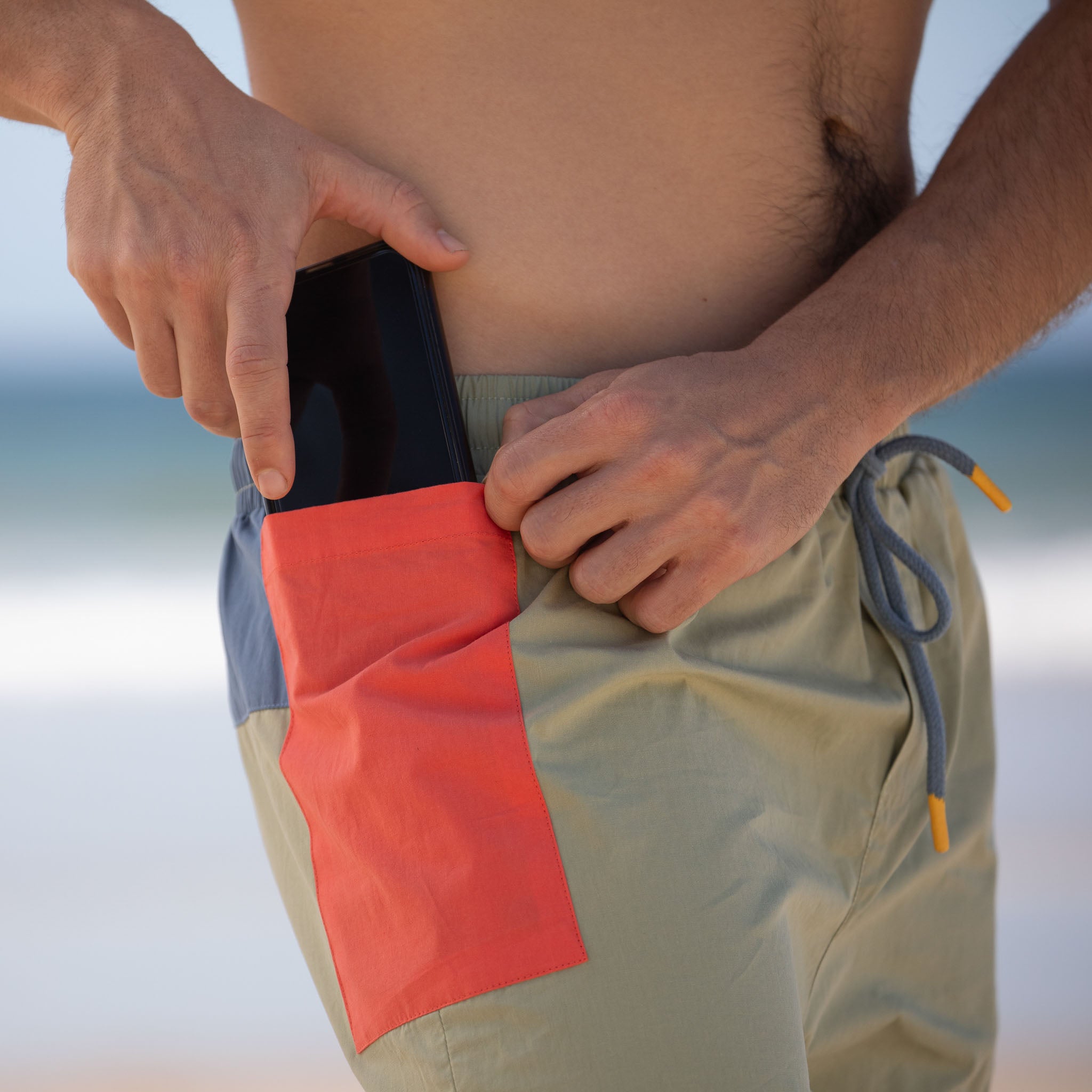 all-groups Man wearing mens beach shorts with red inner liner putting phone into pocket. 